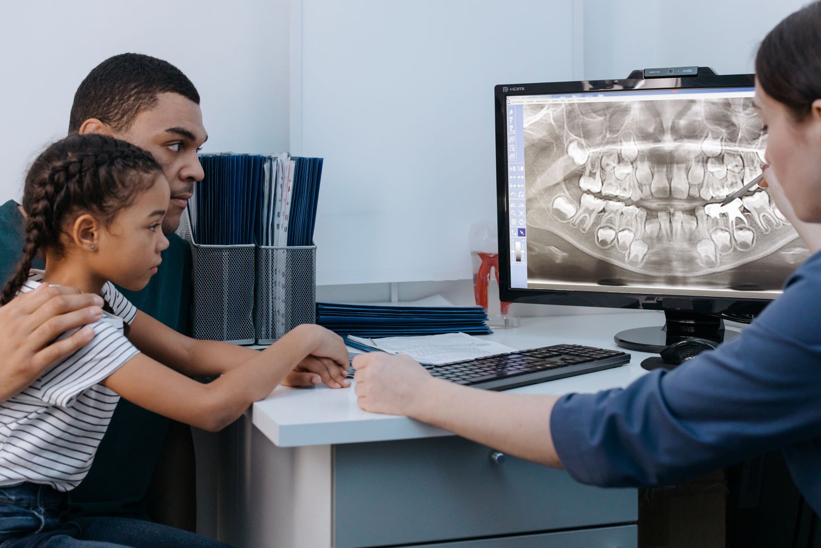 A dentist reviewing a dental X-ray on screen with a parent and child